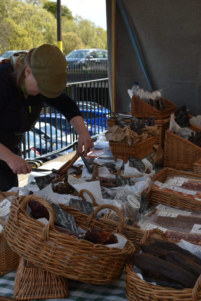 Person arranging baskets of packaged goods at an outdoor market stall, with wicker baskets on a table—a scene reminiscent of the vibrant local markets among the best attractions Edinburgh has to offer.