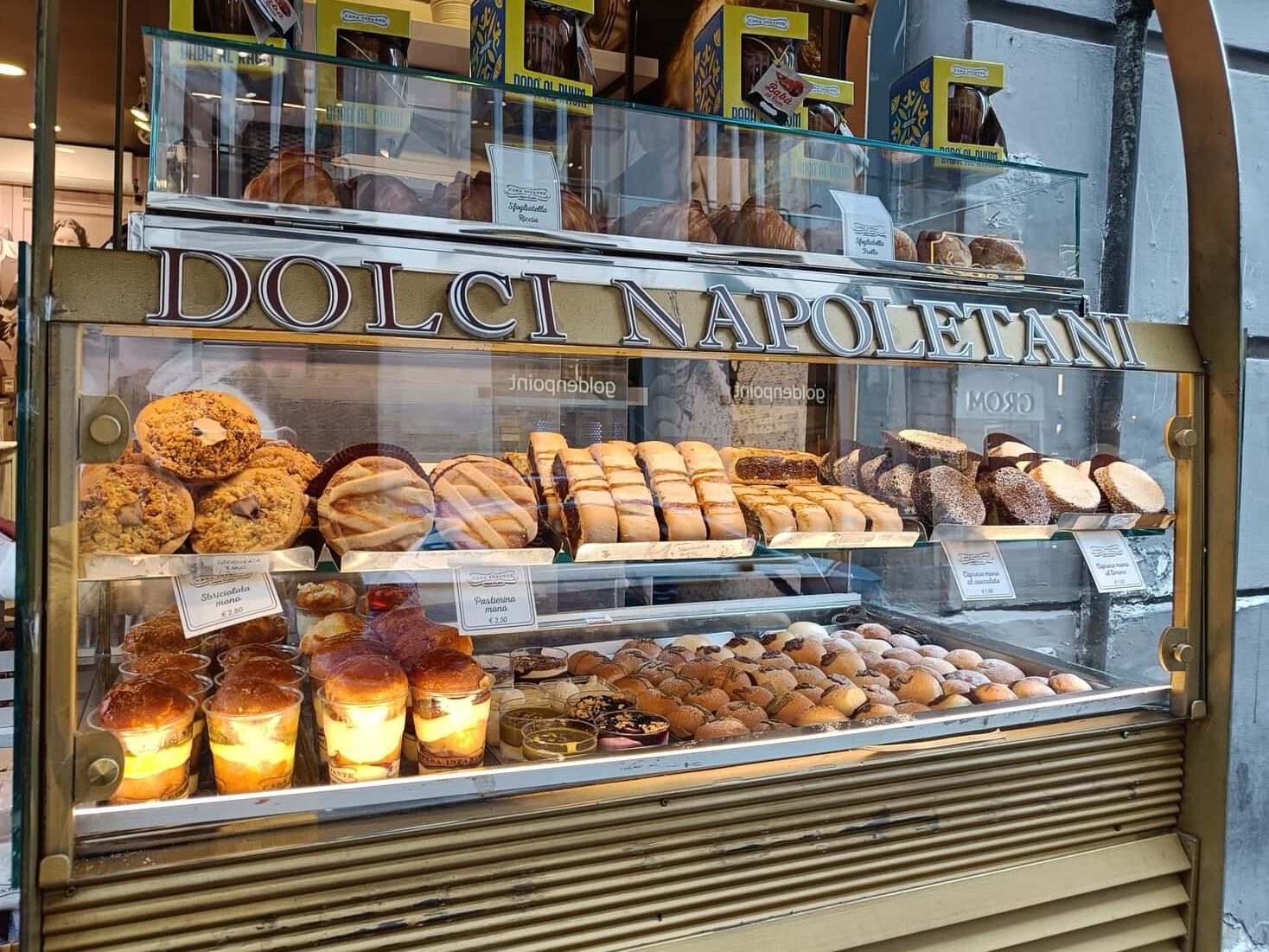 A bakery display with assorted Neapolitan pastries and breads behind a glass case labeled "Dolci Napoletani," perfect for a Naples-inspired breakfast or to pair with your morning coffee.