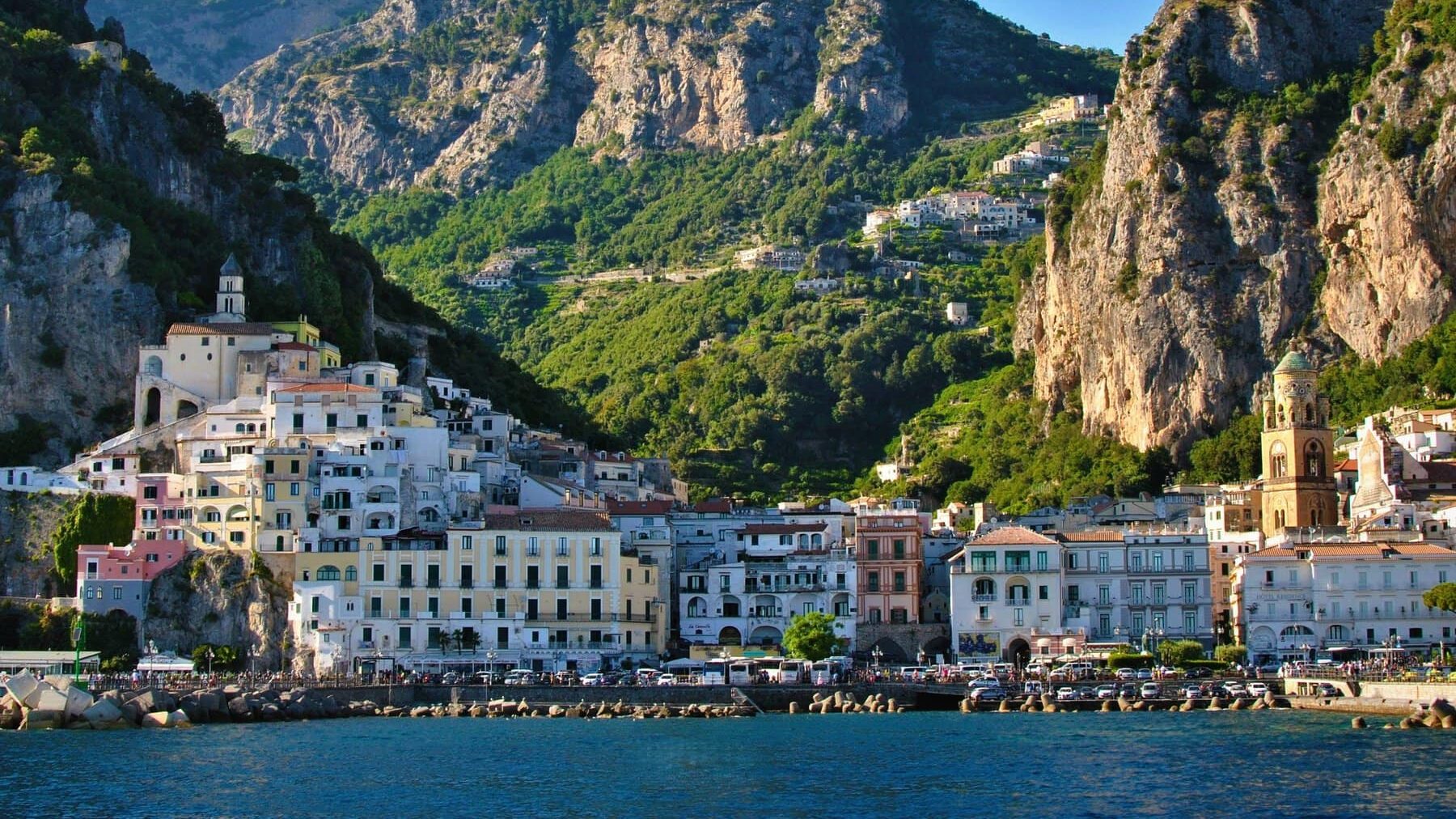 Coastal town with colorful buildings nestled between steep green mountains and the blue sea under a clear sky—one of the best day trips from Naples.