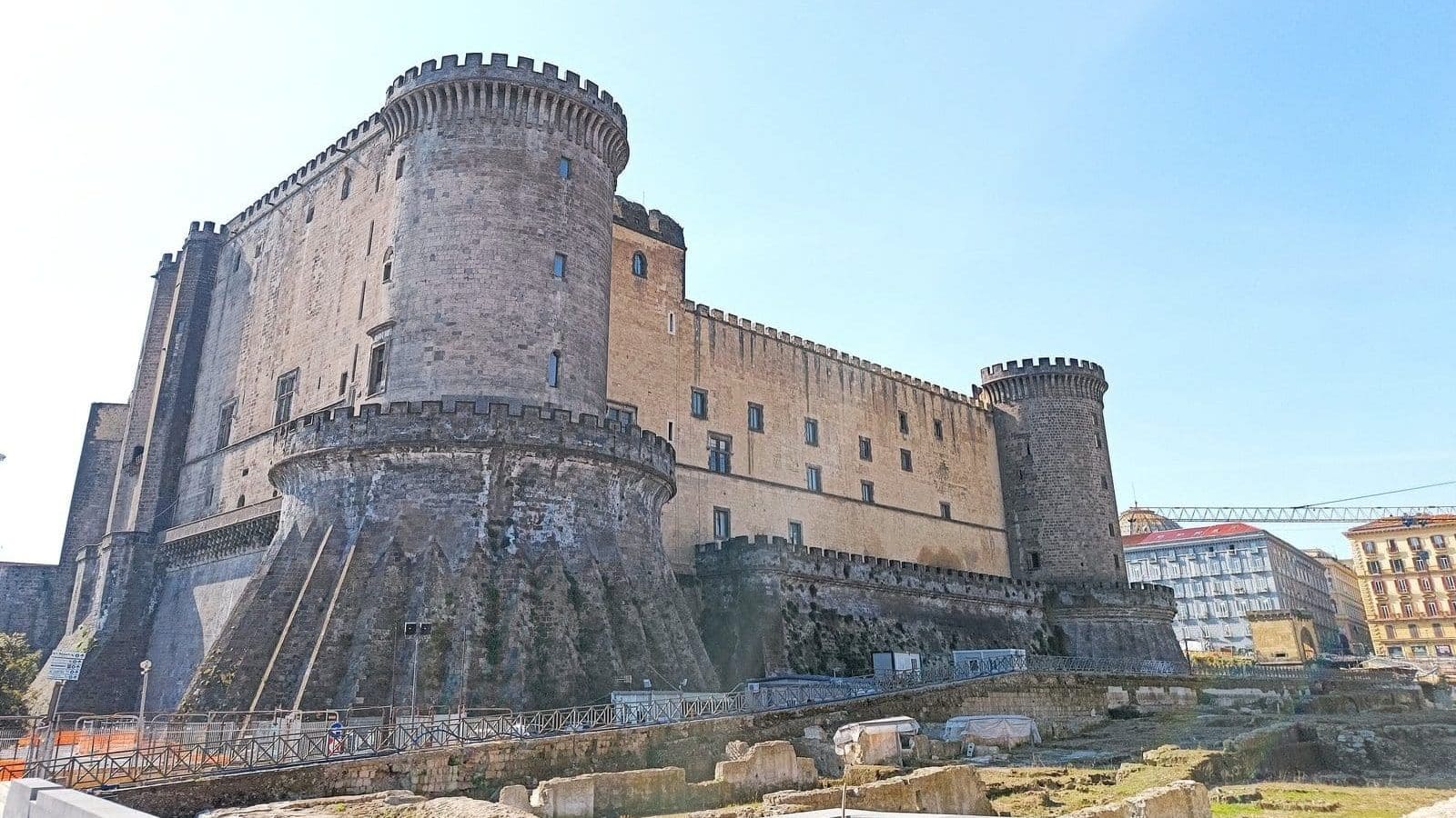 A large stone medieval castle with round towers under a clear blue sky, this landmark is one of the best attractions in Naples for visitors seeking history and stunning views.