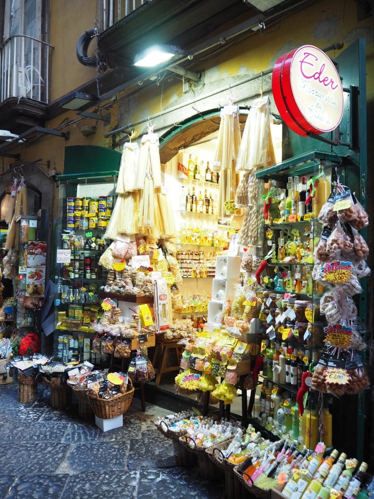 Colorful Italian shop with pasta, bottles, and snacks displayed outside on a cobblestone street—perfect for discovering unique Naples attractions and immersing yourself in local things to do in Naples.