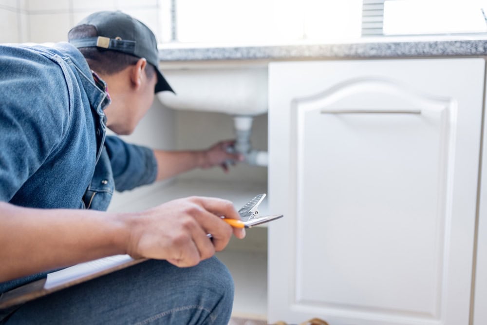 Plumber inspects kitchen sink pipes for leaks, tools in hand and ready for repair.