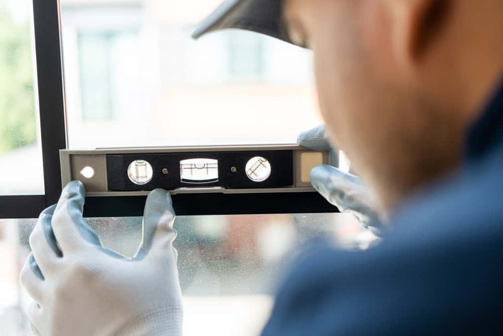 A worker carefully levels a window frame with a spirit level, ensuring precision in the installation.