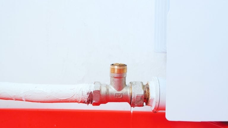 A close-up of a white-painted pipe connected to a radiator with a brass fitting.