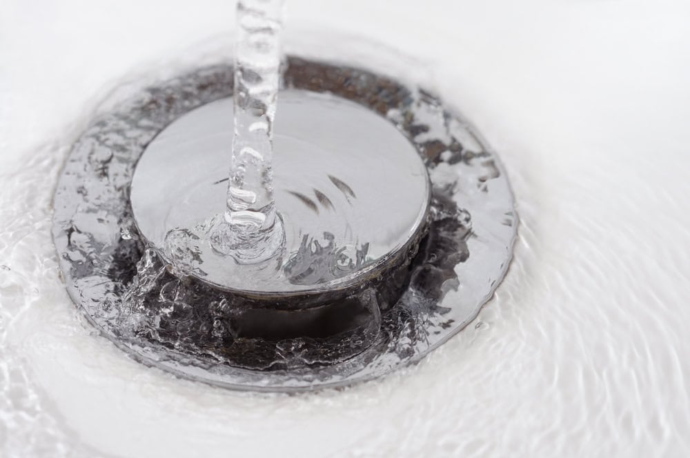 Water flows over a closed metal drain in a white sink.