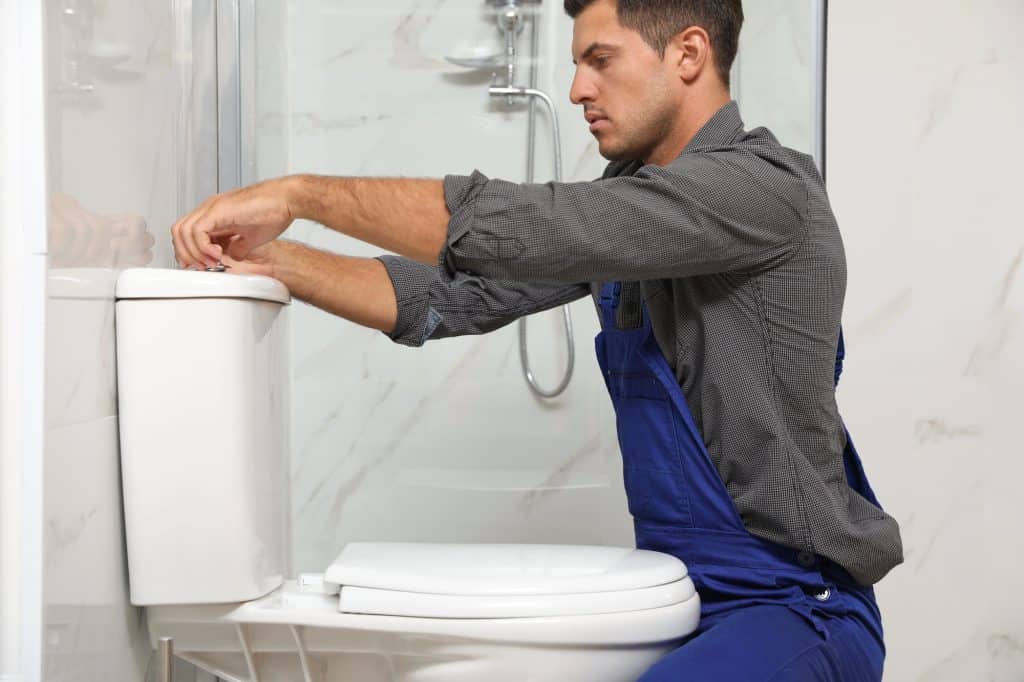 Professional plumber fixing a toilet in a modern bathroom.