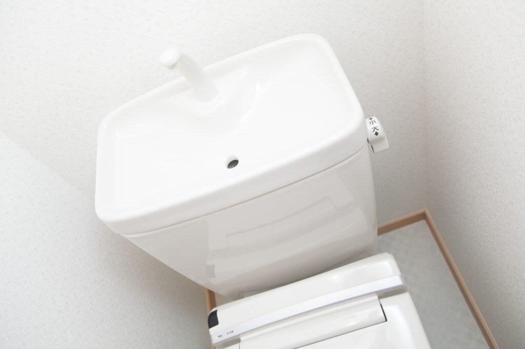 A sleek, modern toilet with a unique top-mounted flush tank in a minimalist bathroom.