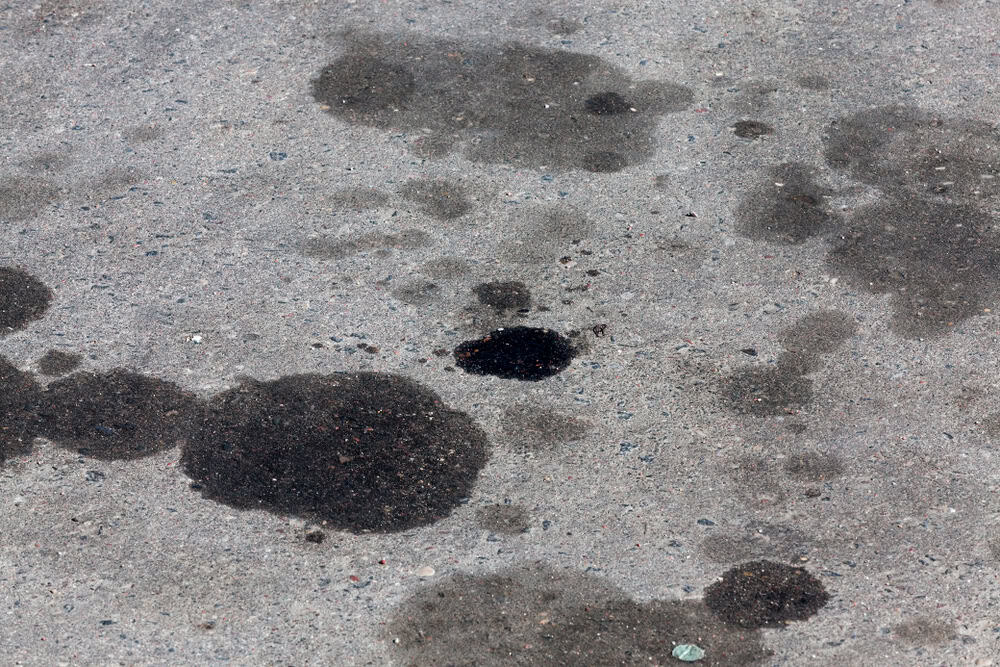 Dark oil stains scatter across a sunlit concrete surface, hinting at the passage of countless vehicles.