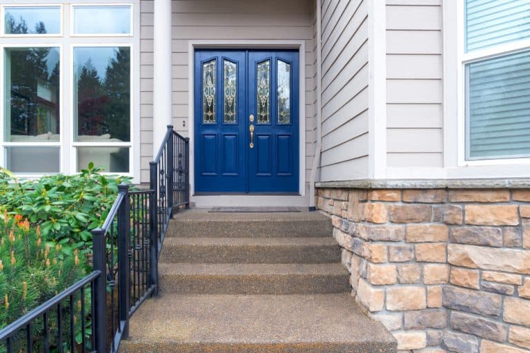 Inviting entryway with bold blue double doors, classic iron railings, and stone accents.
