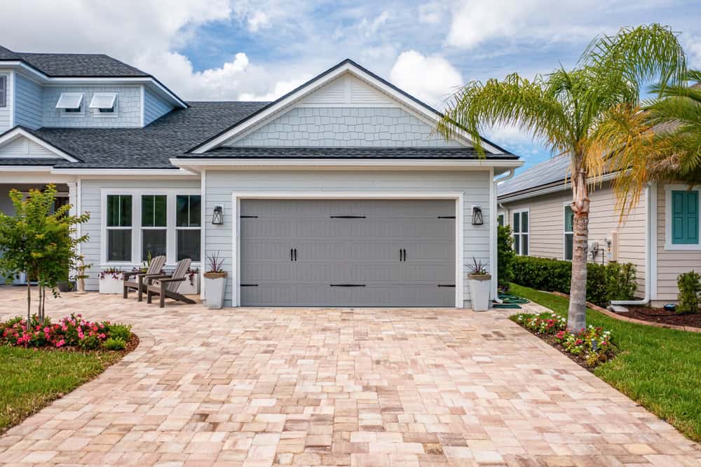 A charming coastal-style home with a beautifully paved driveway, tropical landscaping, and inviting outdoor seating.
