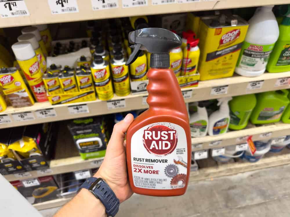 A shopper holds a bottle of Rust Aid rust remover in the cleaning products aisle of a hardware store.