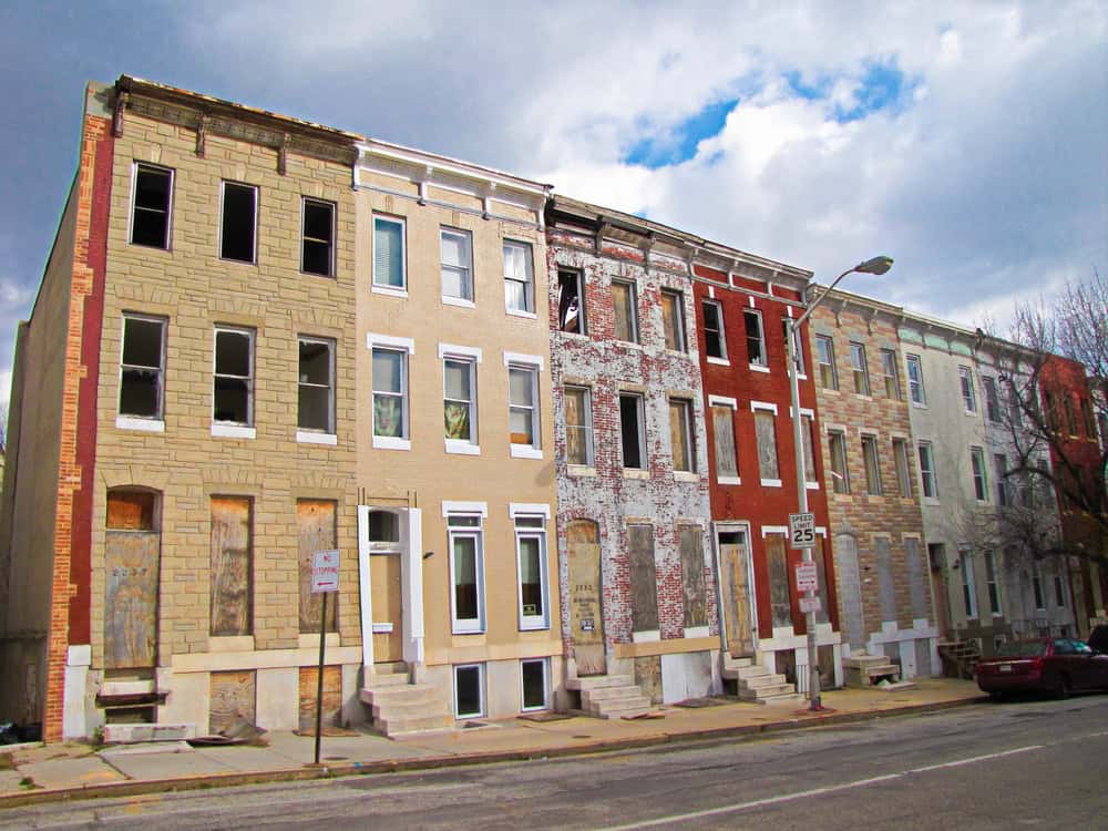 A row of colorful, weathered townhouses stands tall under a partly cloudy sky, hinting at the passage of time and urban decay.