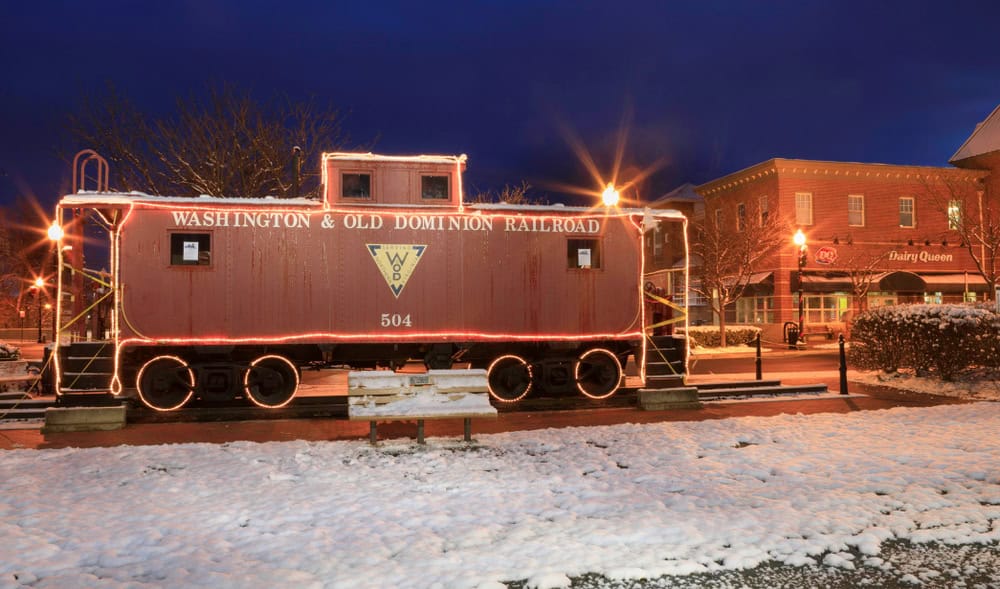 A beautifully lit Washington & Old Dominion Railroad caboose stands in a snowy town square at night.