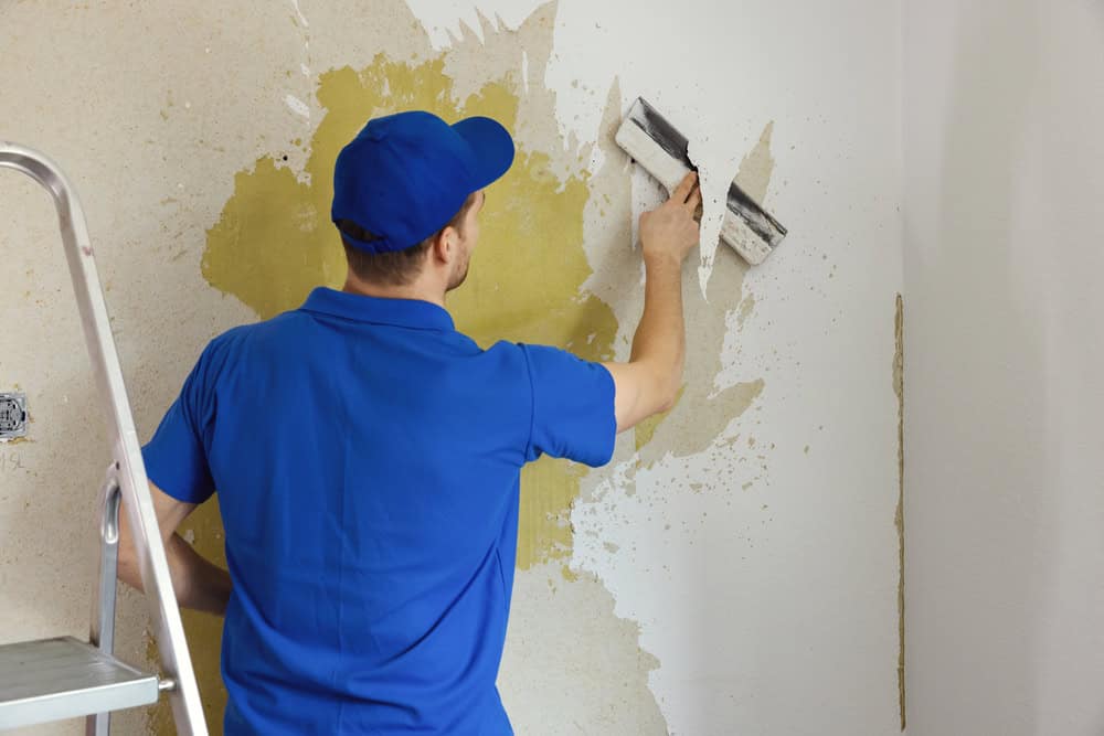 A worker meticulously removes old painted wallpaper, revealing the layers beneath.