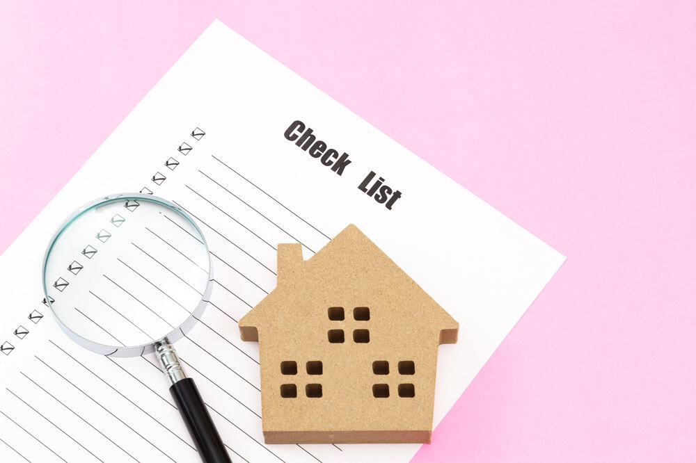 House hunting checklist with a magnifying glass and a wooden house model on a pink background.