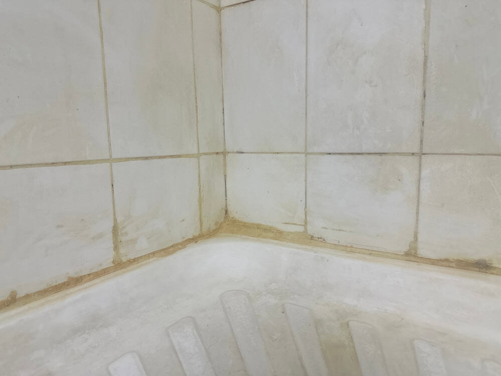 A close-up of a dirty, stained shower corner with discolored tiles and grout.