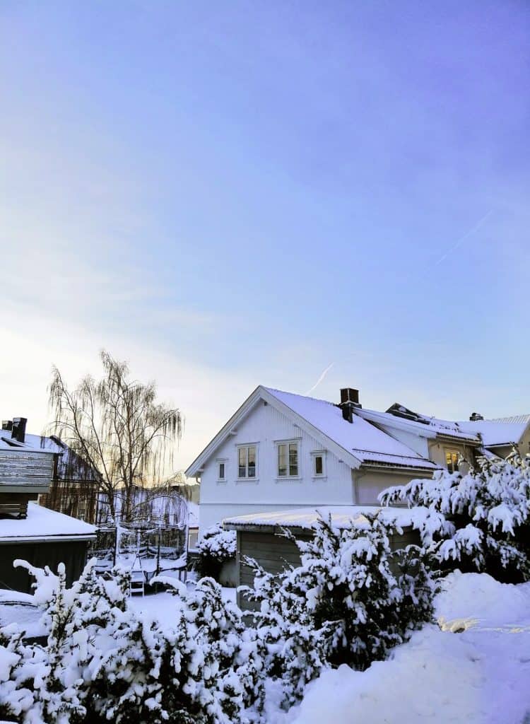 A serene winter morning blankets a cozy white house in glistening snow under a pastel sky.