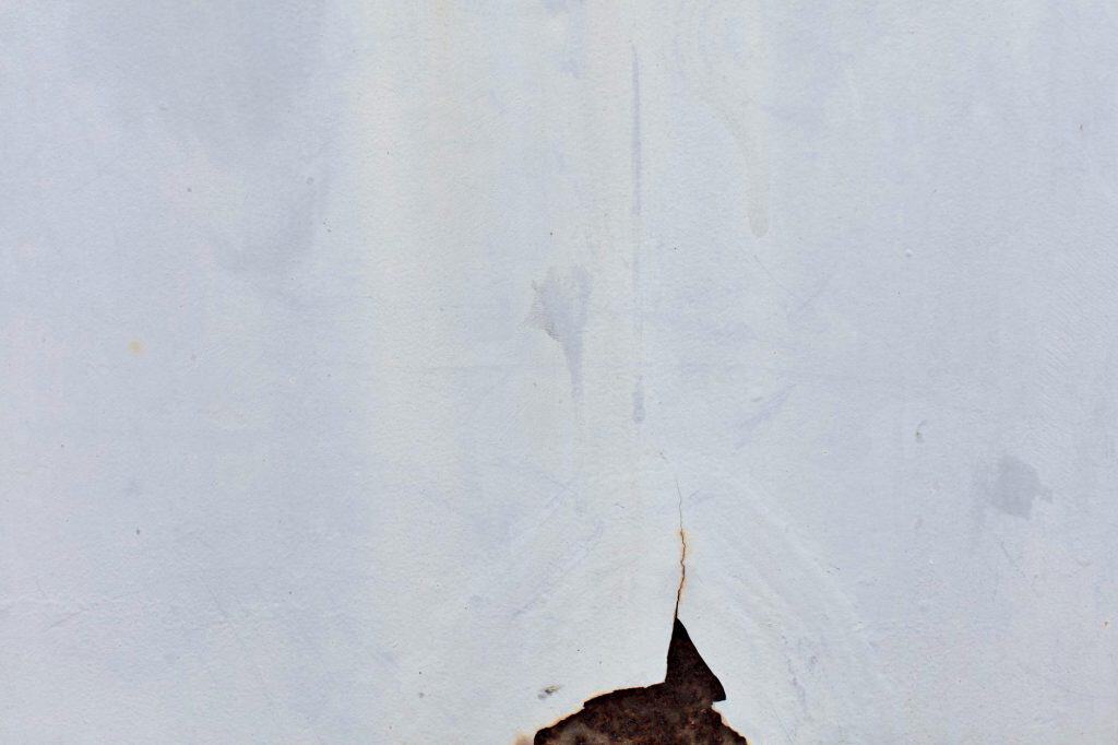 A jagged hole in a white wall reveals darkness beneath, creating a stark contrast between light and shadow