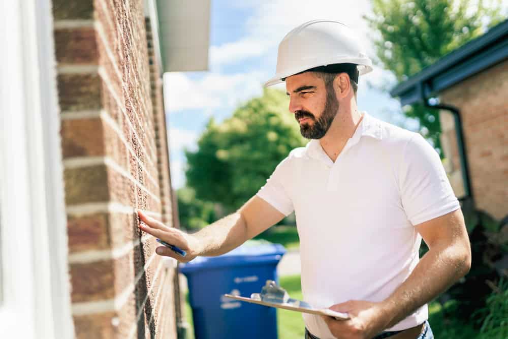 A construction worker inspects a brick wall while holding a clipboard, ensuring quality and precision on the job site.