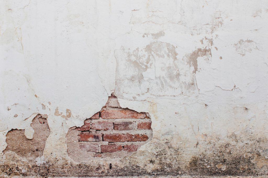 Weathered wall with peeling paint and visible brickwork; rustic architectural detail.