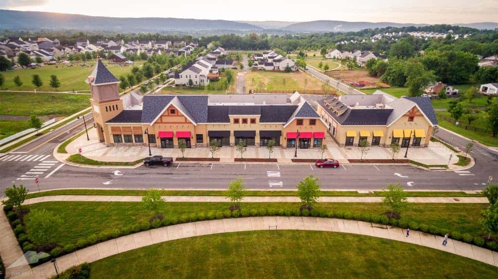 Charming suburban shopping plaza nestled within a serene residential community, framed by picturesque hills in the distance.