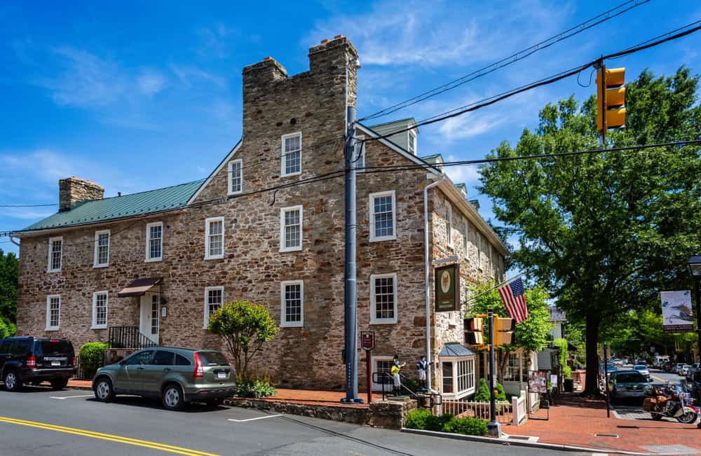 Historic stone building on a charming street, showcasing American flag and parked cars.