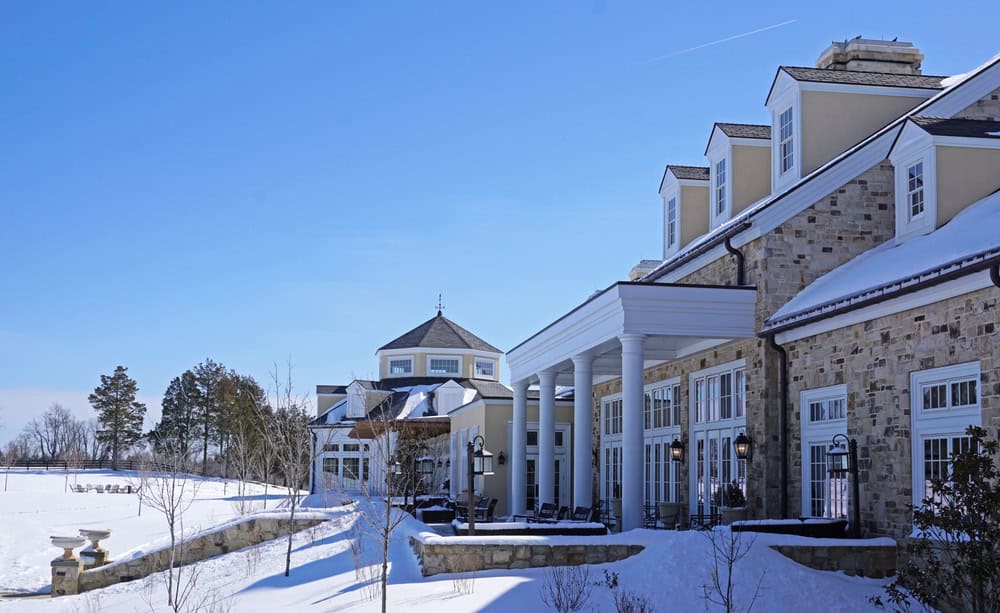 A grand estate wrapped in winter’s embrace, basking under a crystal-clear blue sky.