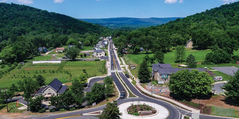Mountain Main Street: A newly renovated road winds through a small valley town, complete with a fresh roundabout and neat sidewalks, surrounded by lush green Appalachian hillsides.