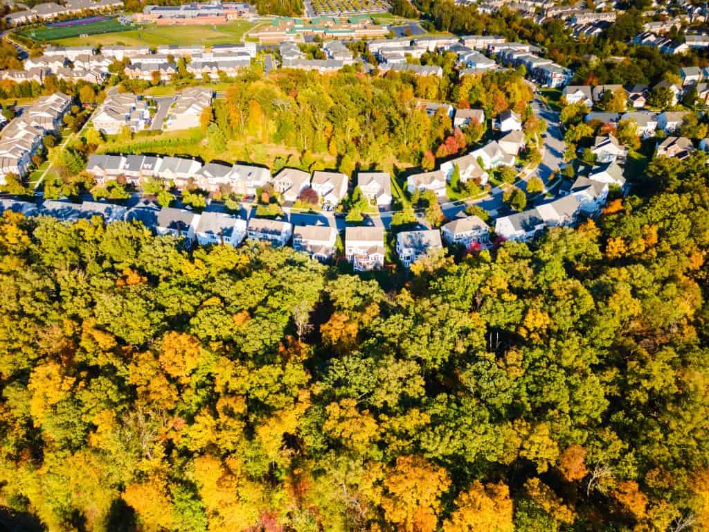 Autumn's Embrace: Aerial view of a suburban neighborhood nestled among vibrant fall foliage, with sports fields visible in the distance.