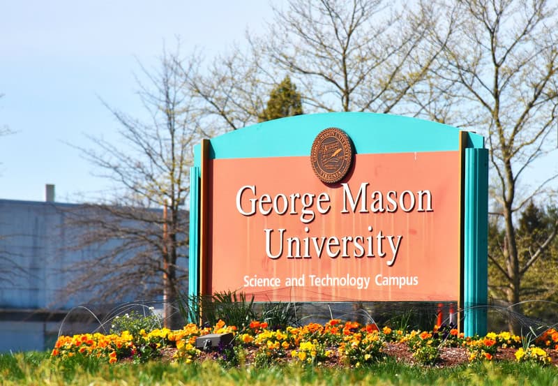 Welcome to George Mason University's Science and Technology Campus, marked by its signature coral and turquoise sign surrounded by vibrant spring flowers.