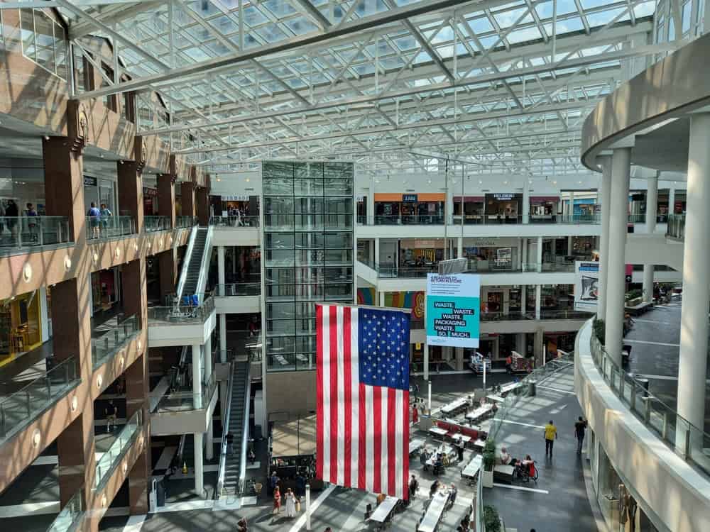 A vibrant afternoon in the Mall of America, showcasing its expansive interior with a towering American flag and sunlight streaming through the glass ceiling.