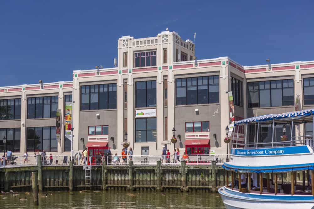 Alexandria VAHistoric Waterfront Comes Alive: Art Deco building hosts bustling riverside activity, as Potomac Riverboat Company vessel awaits passengers for scenic tours along Washington D.C.'s vibrant harbor.