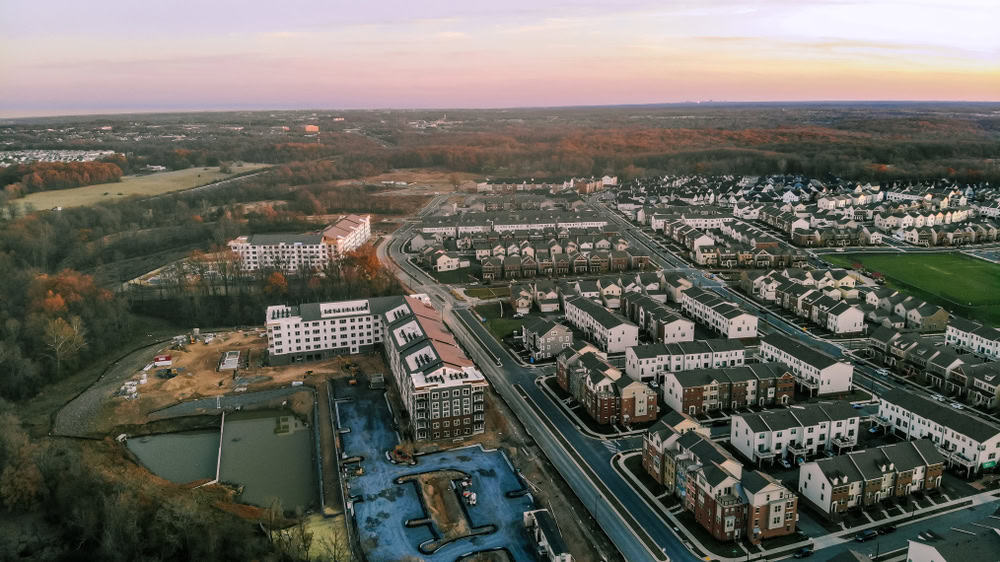 Aerial view of suburban neighborhood expansion at sunset, featuring new apartment complexes and surrounding greenery.