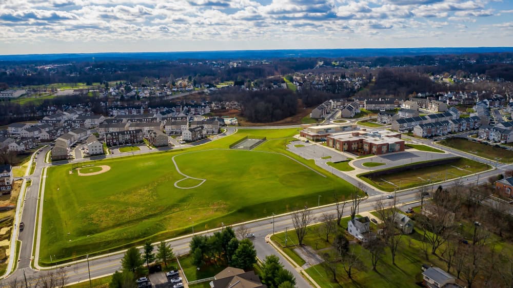 Aerial view of a suburban neighborhood with a school and sports fields on a bright, partly cloudy day.