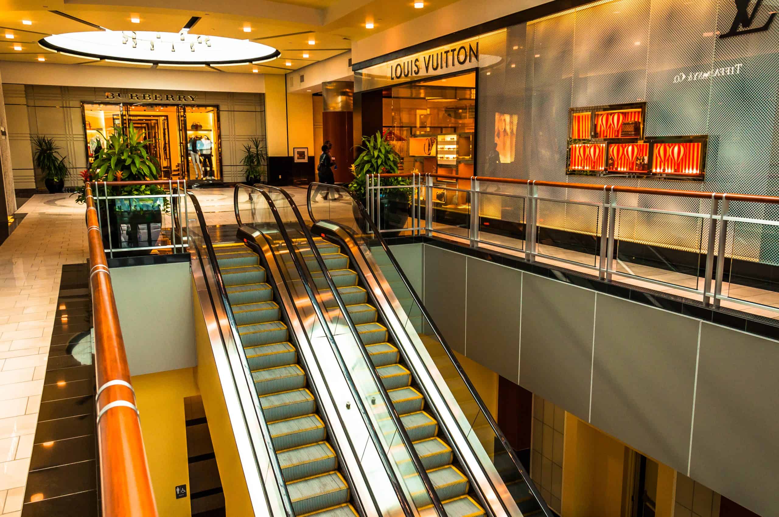Escalators lead to luxury shopping with Burberry and Louis Vuitton boutiques in a high-end mall.