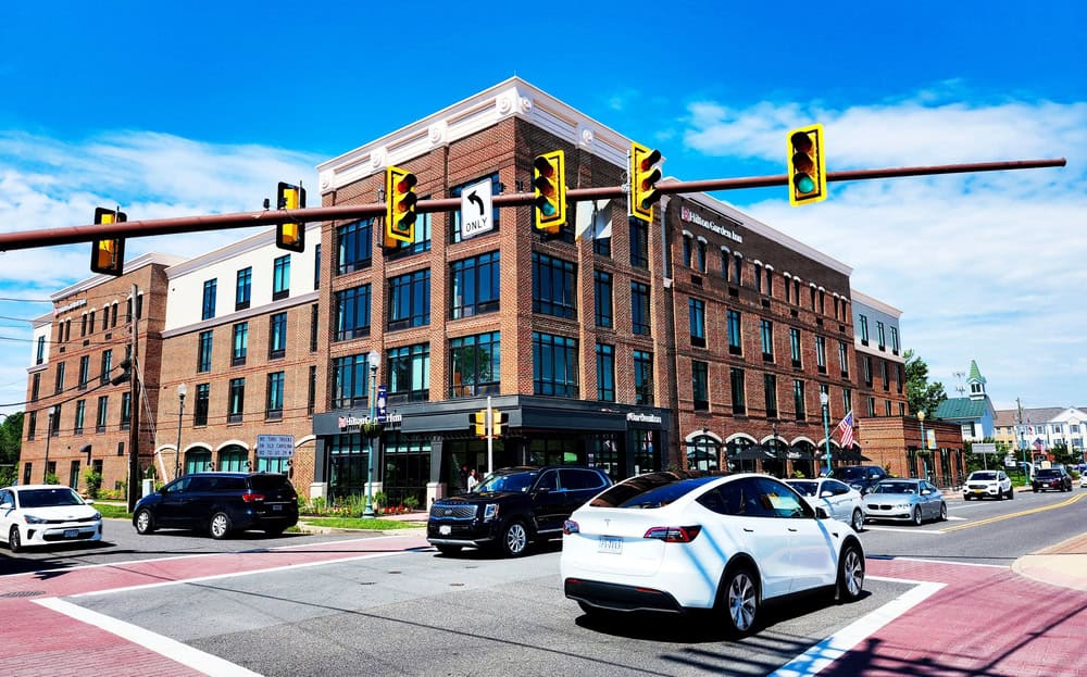 Busy urban corner with sleek modern brick buildings and diverse traffic under a bright blue sky.