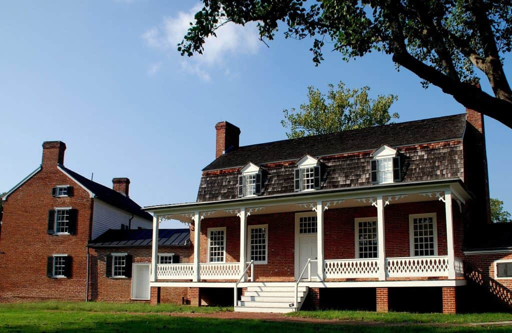 Charming historic red brick colonial house with a white porch, basking in the afternoon sun.