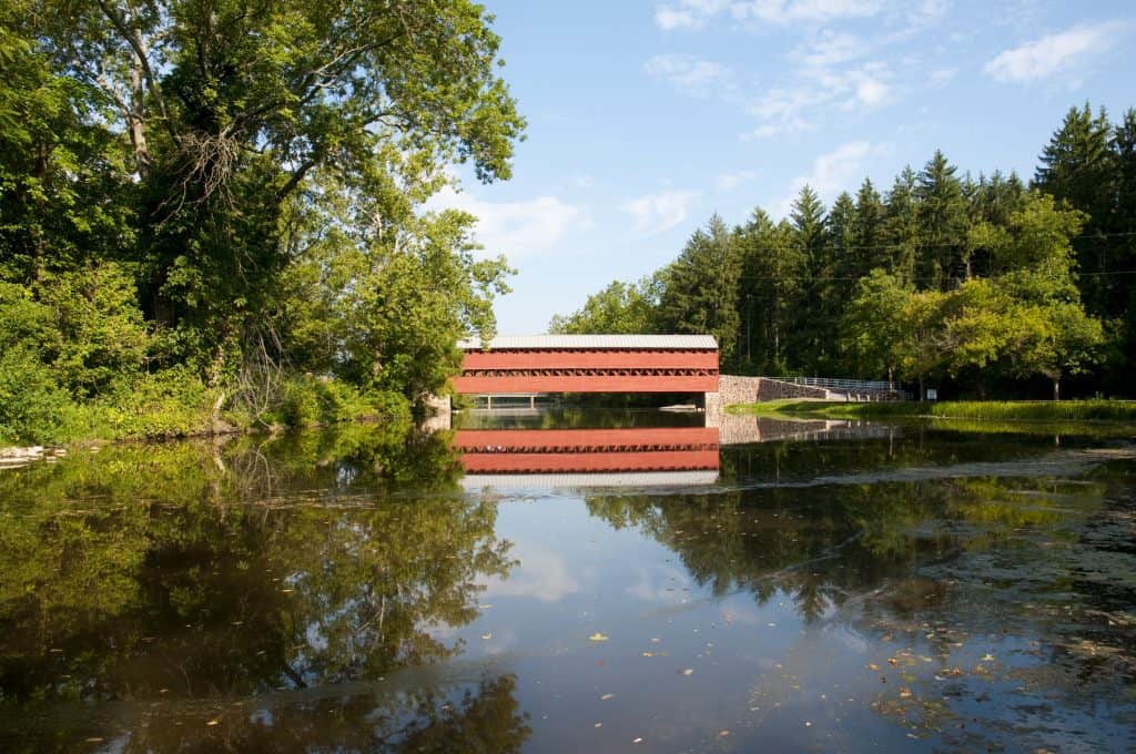 Red covered bridge over calm forest river.