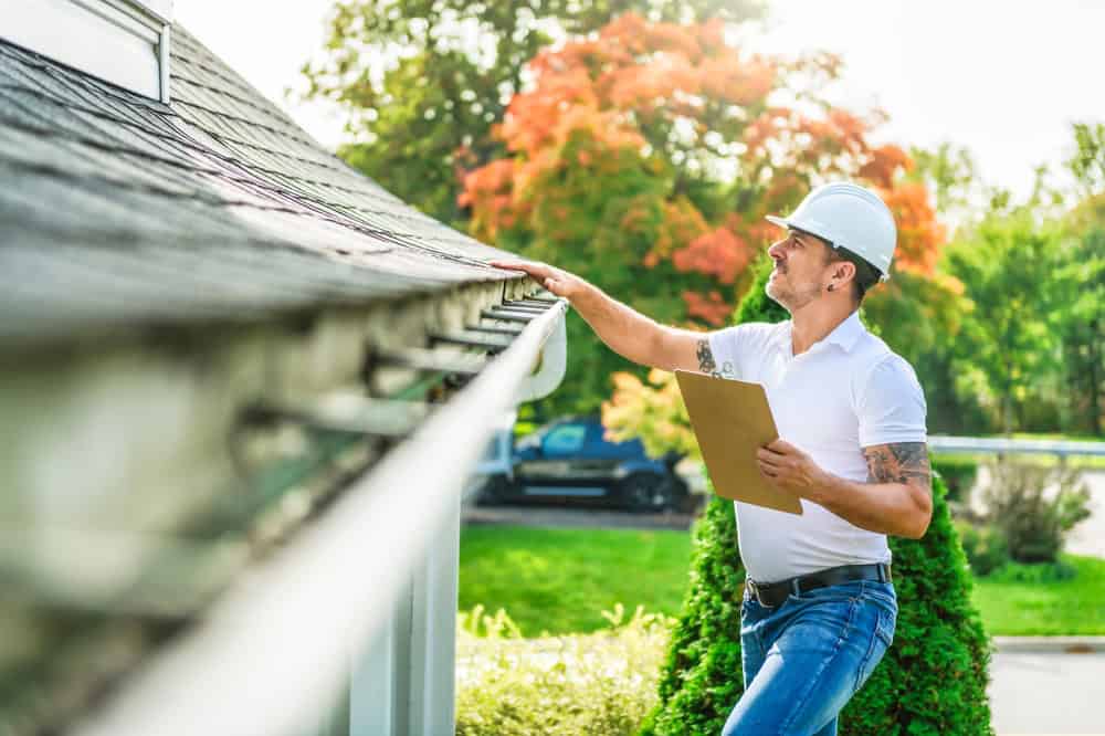 Home inspector examining roof gutters during autumn, clipboard in hand, ensuring proper drainage before the season changes.