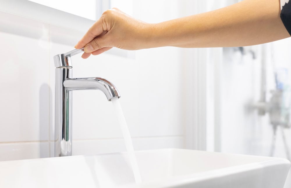 Close-up of a hand testing a modern bathroom faucet for water pressure and leaks during a professional home plumbing inspection by Next Day Inspect.