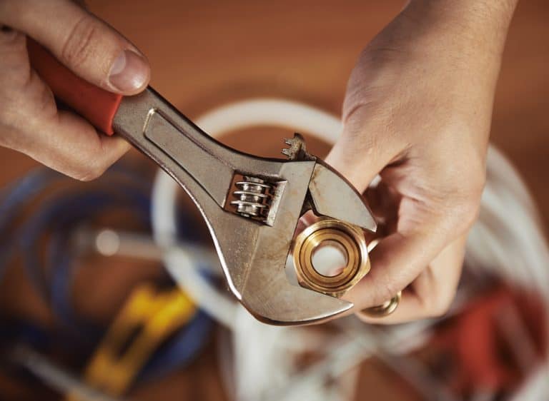 Hand using wrench on plumbing fitting.
