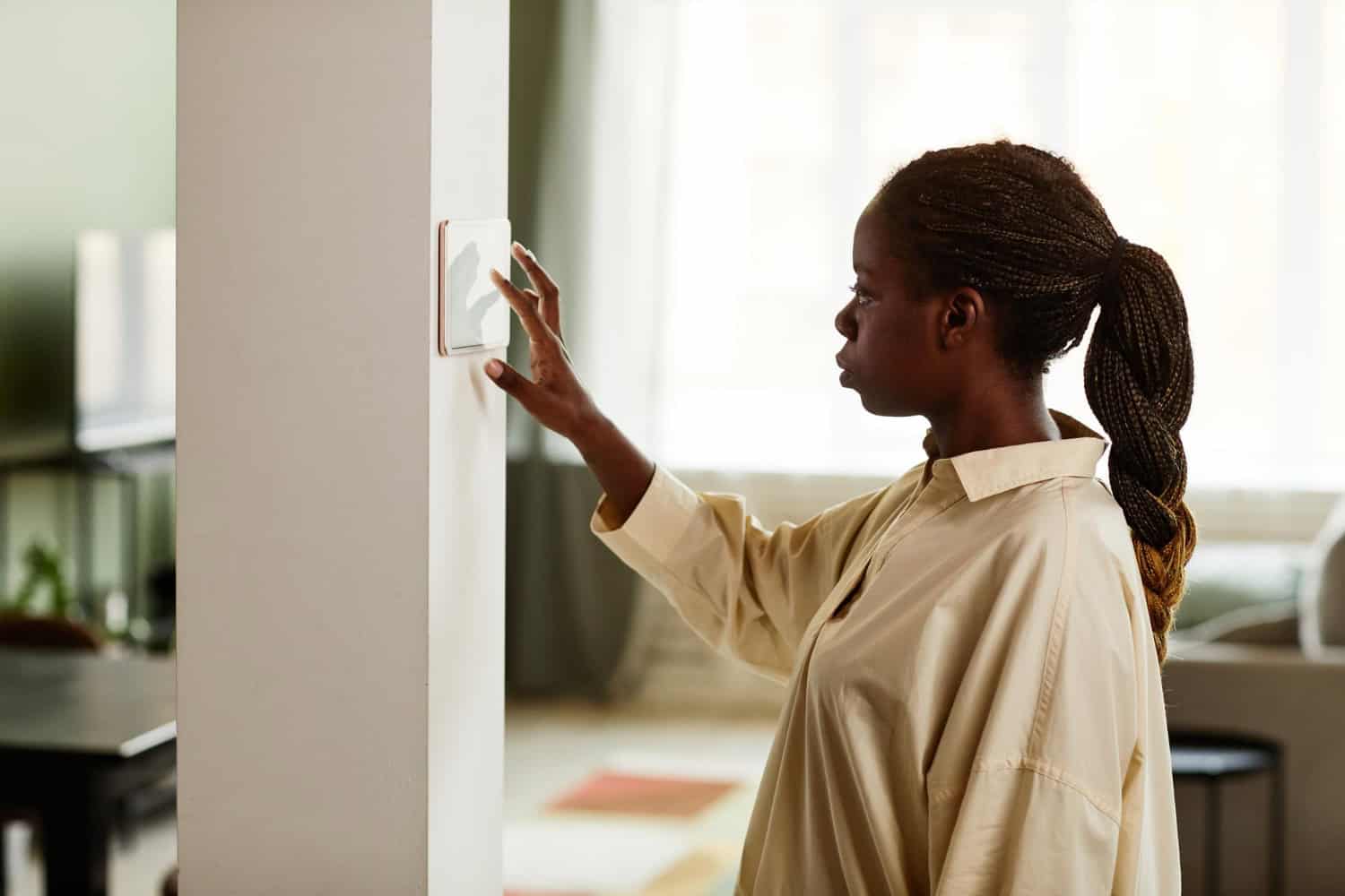 A young woman adjusts the smart thermostat in her modern home.