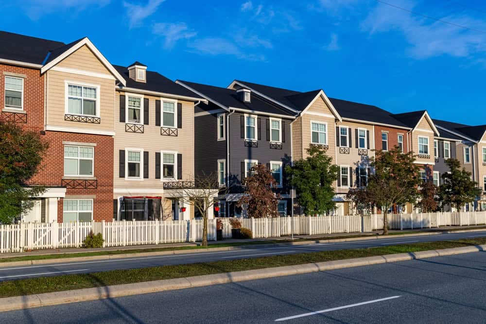 Charming row of modern townhomes with white picket fences on a sunny suburban street.