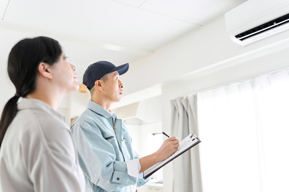 A technician inspects a wall-mounted air conditioner while a homeowner looks on, ensuring efficient climate control at home.