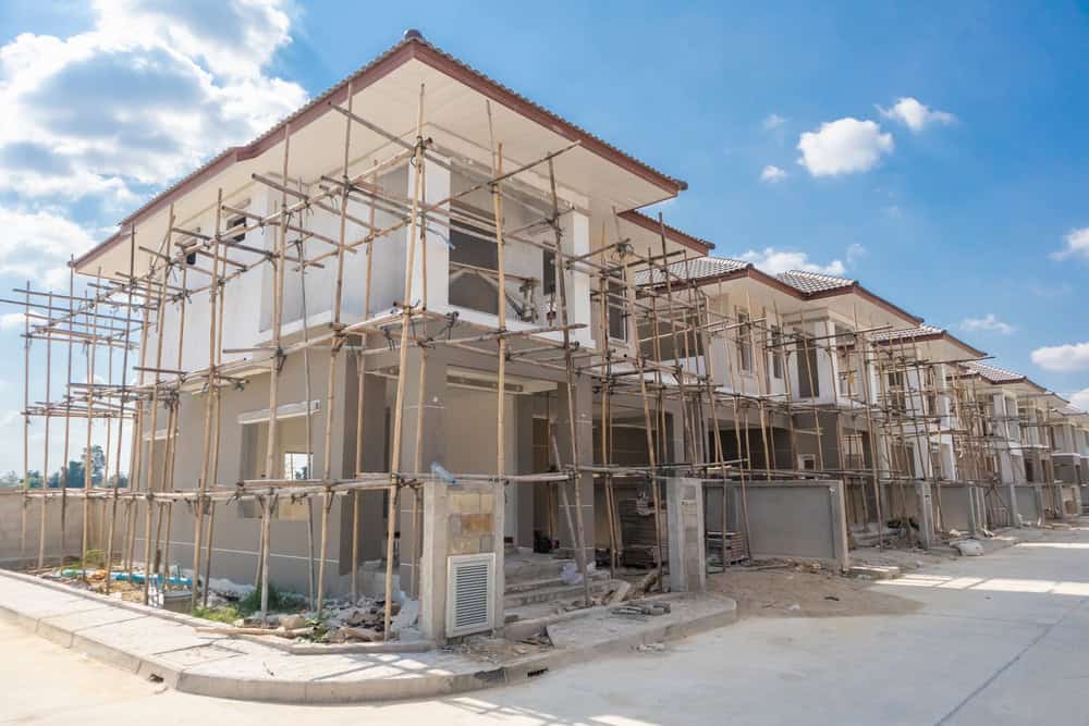 New modern townhouses under construction, surrounded by scaffolding on a sunny day.