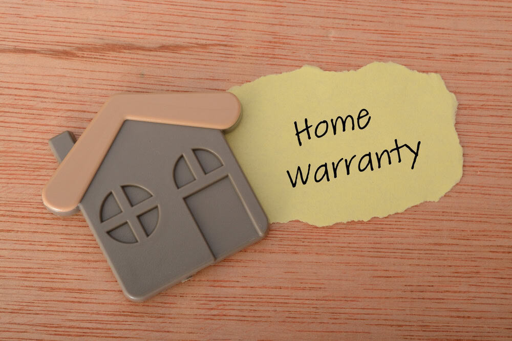 Home warranty concept with a house-shaped magnet and handwritten note on wood.