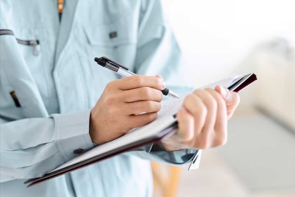 Inspector in a light blue uniform fills out a report on a clipboard.