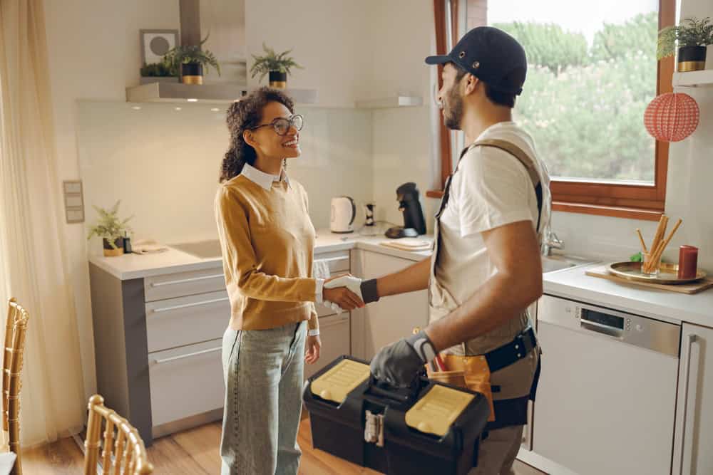 A homeowner warmly greets a handyman in her modern kitchen, ready for home repairs.