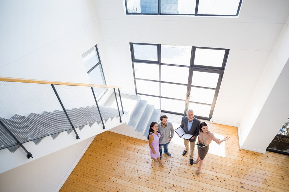 A real estate agent shows an enthusiastic couple the spacious entryway of a modern home, highlighting its bright and open design.