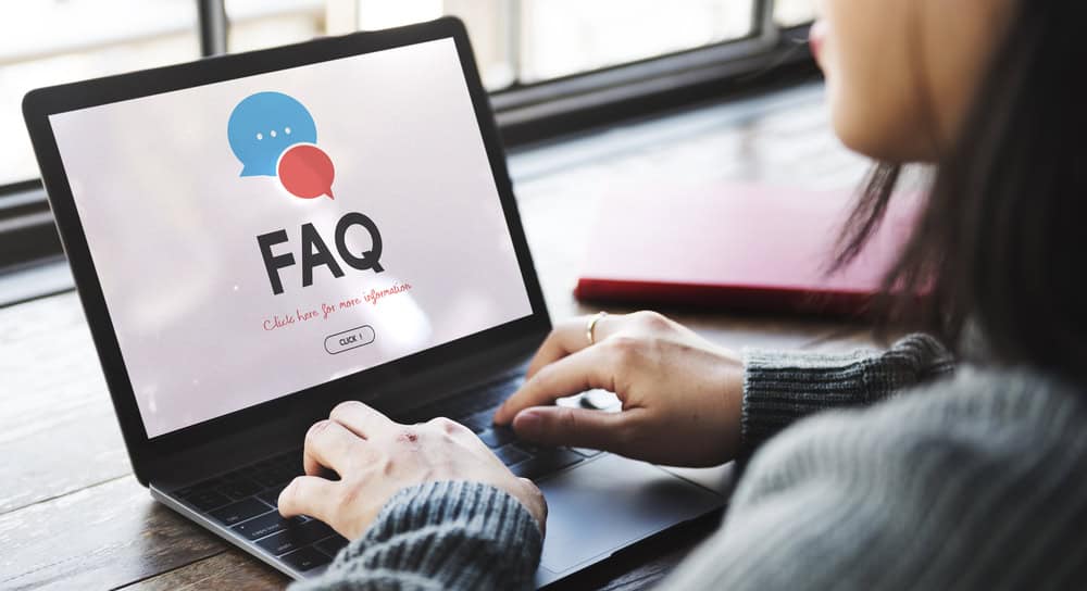 A woman browses an FAQ page on her laptop, seeking answers online by a sunlit window.